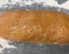 Step <p>Vierte la masa en la superficie de trabajo espolvoreada con harina y forma un cilindro de aprox. 22 cm de largo. Colócalo en la bandeja de horno y pincélalo con leche.</p><p><br></p> illustration